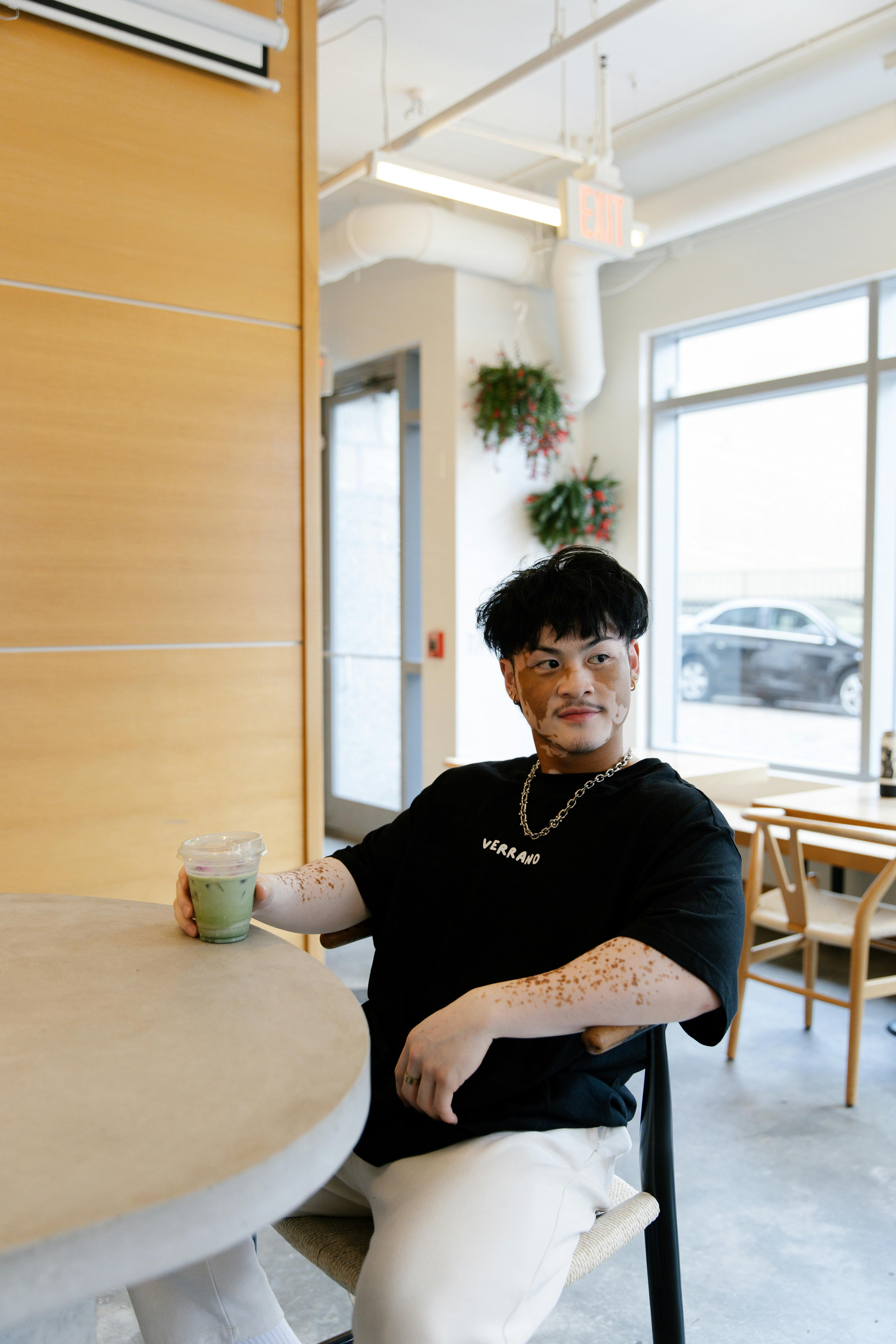 Individual enjoying a matcha latte in a stylish, modern café interior with natural lighting.
