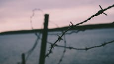 日落时分，铁丝网与宁静海滩的戏剧性特写，在模糊背景的衬托下更显宁静