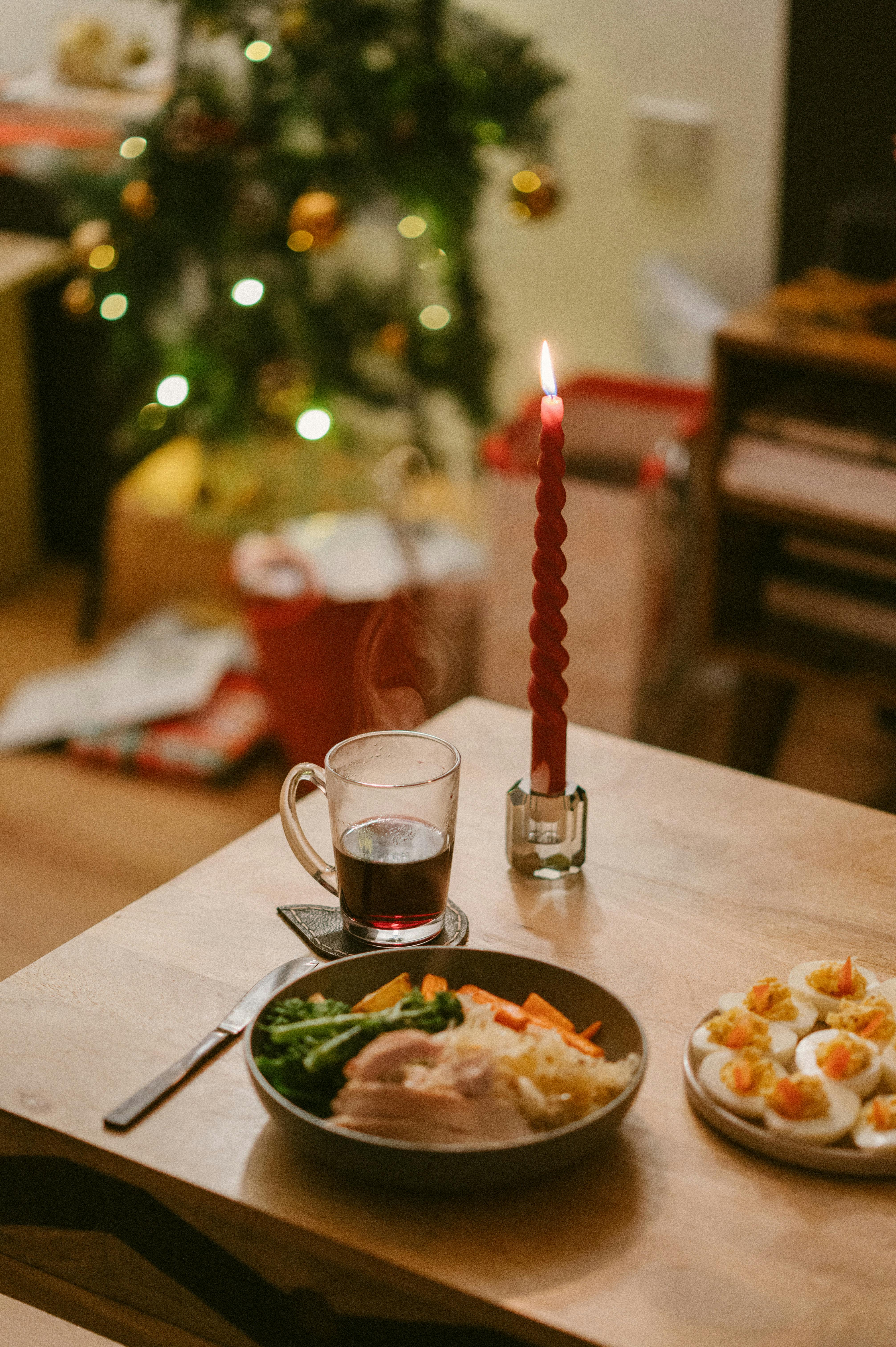 Warm and festive Christmas dinner setup with a lit candle and decorated tree.