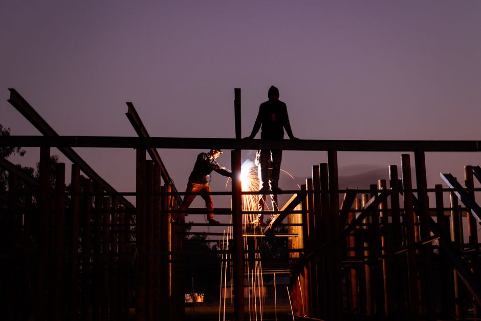 Silhouettes of welders working at a construction site during sunset, creating dramatic sparks.