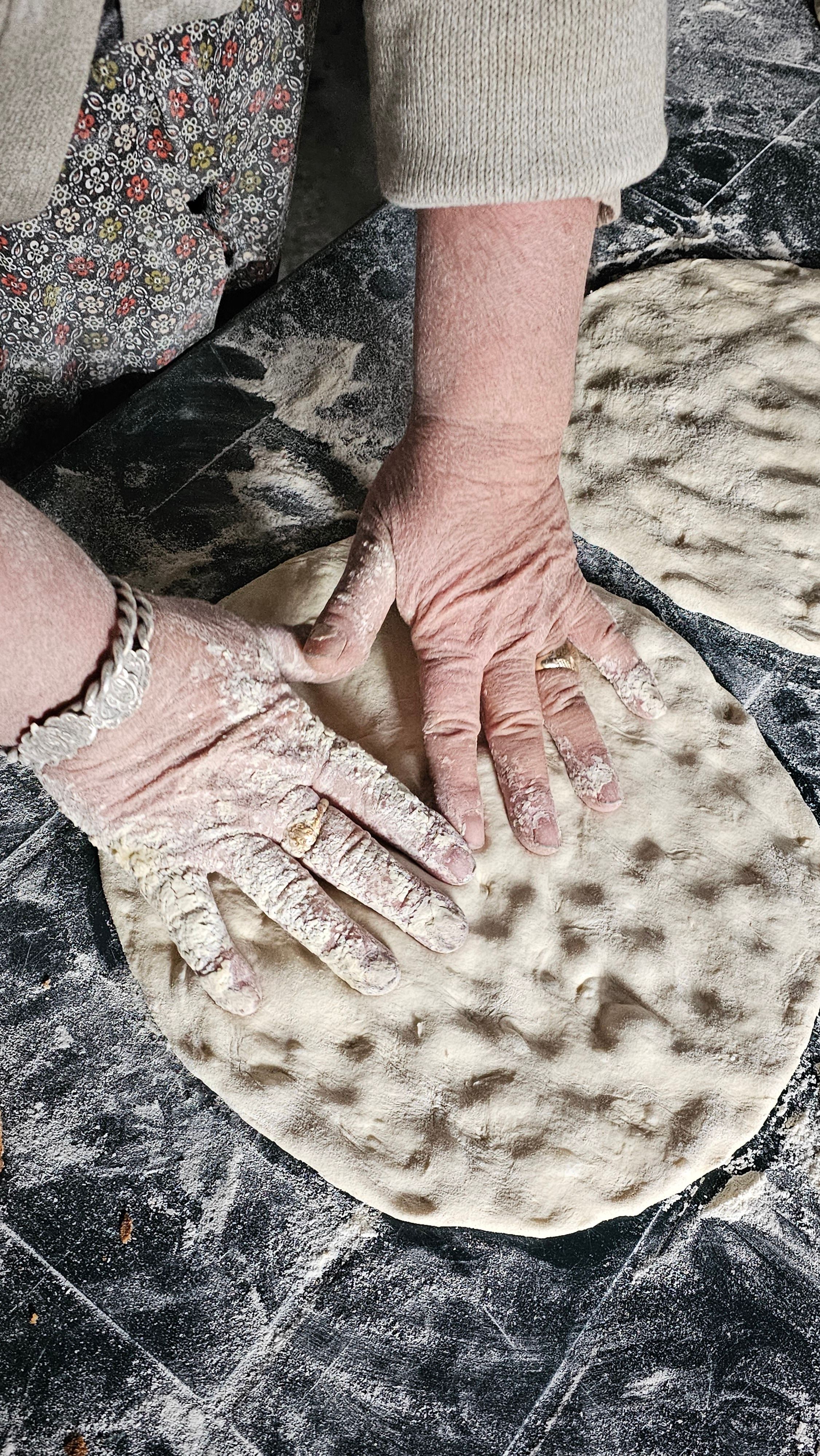 Hands stretching and shaping pizza dough on a wooden surface`