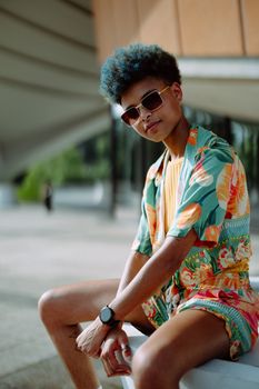Young man wearing colorful summer shirt and shorts seated outdoors in Berlin.