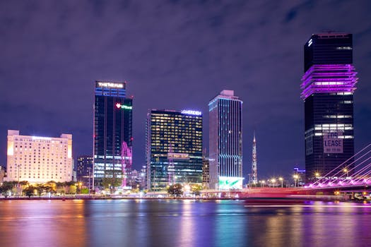 Stunning nighttime view of modern skyscrapers reflecting lights across a tranquil river scene.