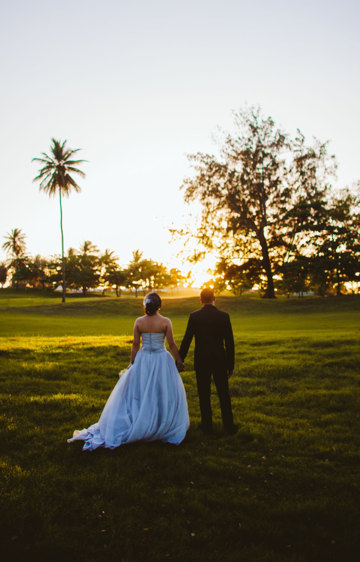 Bride and groom holding hands on a grassy field at sunset