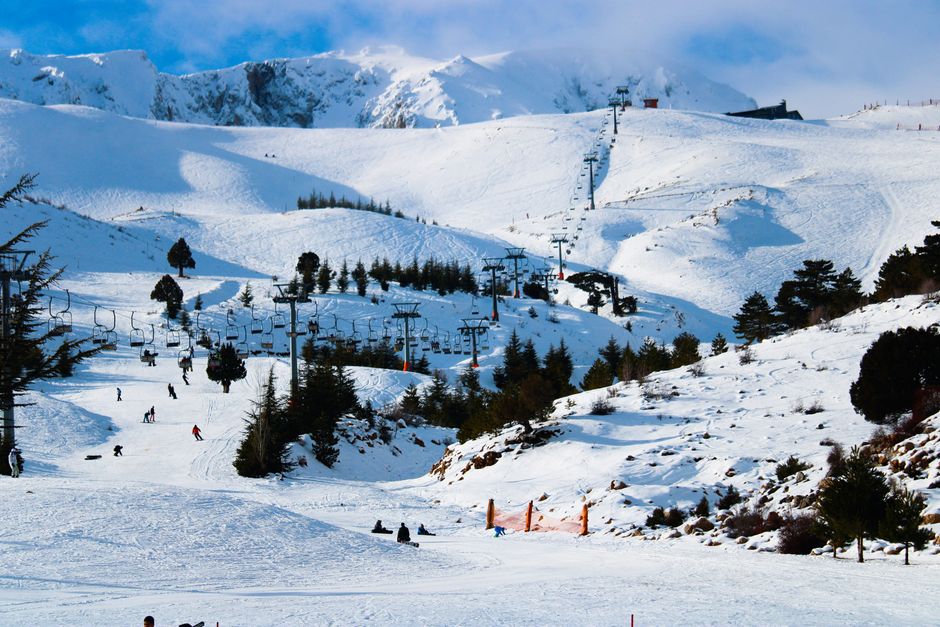 A beautiful winter ski resort featuring snowy mountains, skiers, and chair lifts under a clear blue sky.