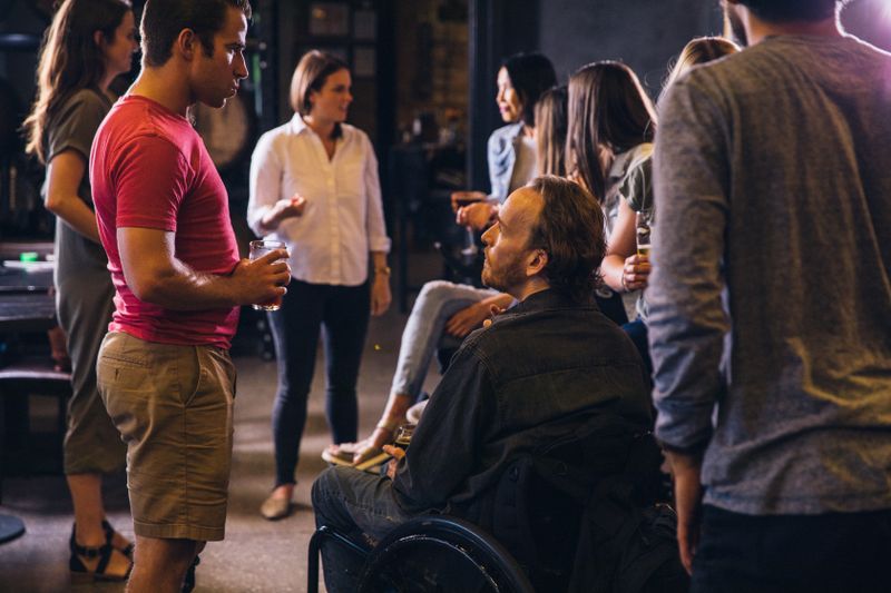 A diverse group of friends with different disabilities, including wheelchairs and prosthetics, laughing together at a community gathering.