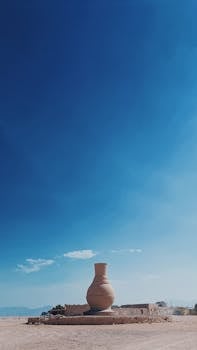 A solitary ancient vase structure stands in a vast desert under a clear blue sky.