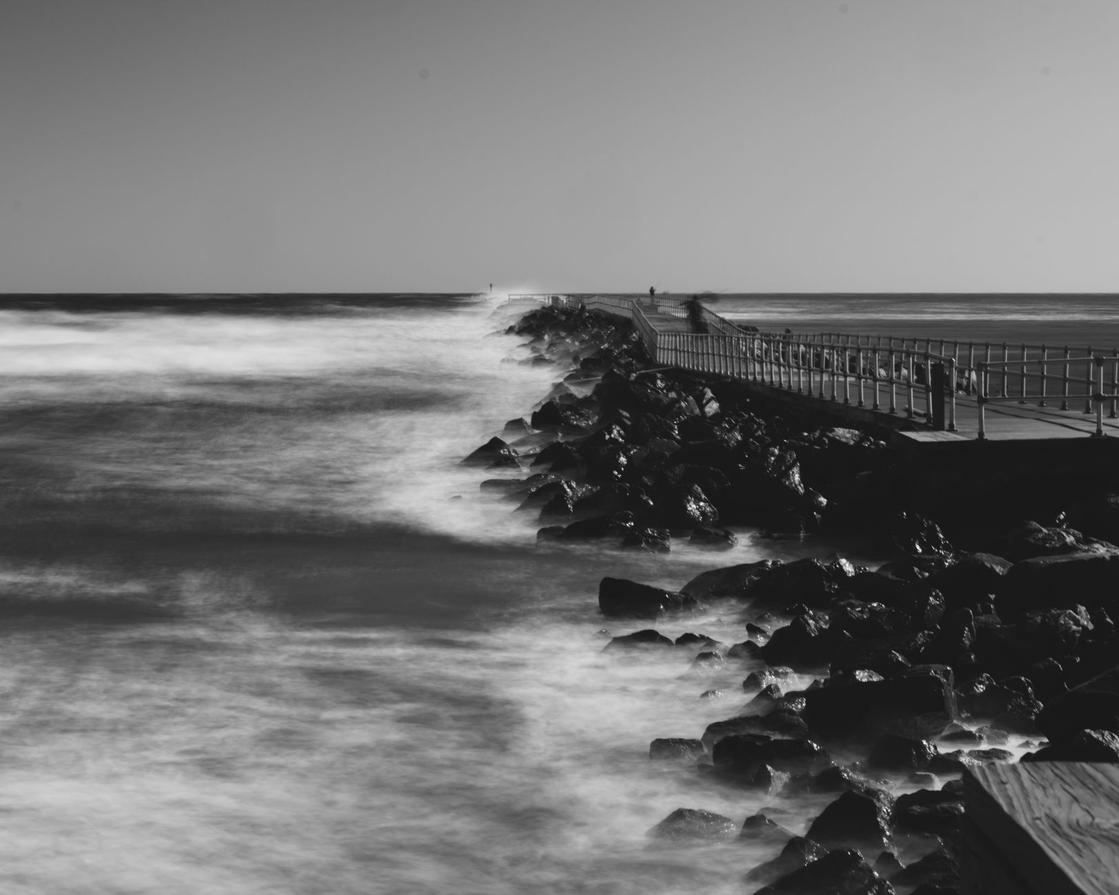 Foto dramática en blanco y negro de olas del océano rompiendo contra un muelle rocoso.