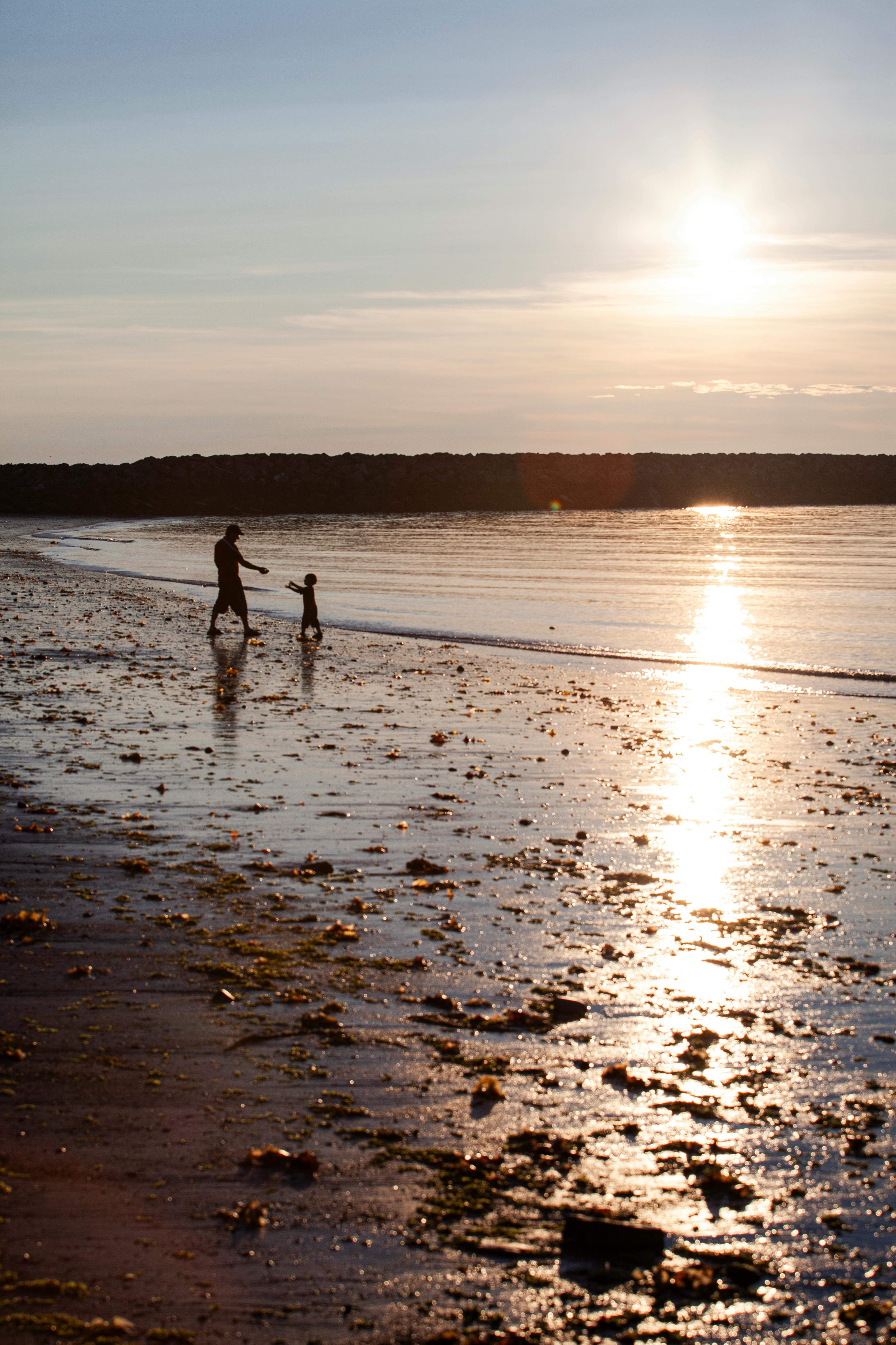A silhouette of a parent and child walking along Rimouski beach at sunset.