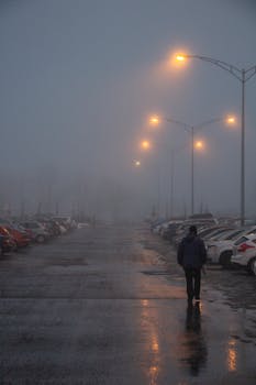A lone figure walks through a foggy parking lot in Québec at night.