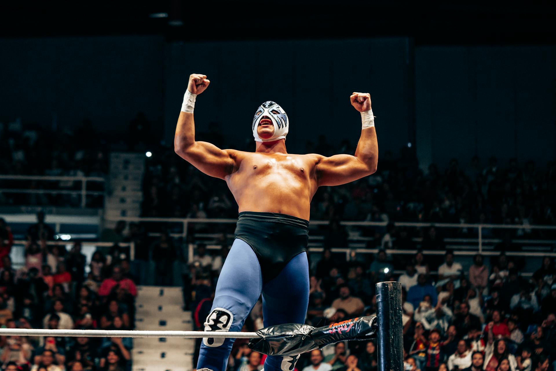 A masked wrestler celebrates victory in a vibrant wrestling arena in Santiago de Querétaro.