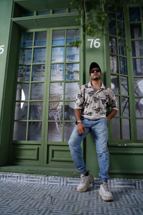 Free Man in casual fashion stands confidently near green windows Stock Photo