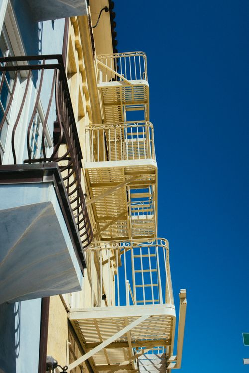 Free Low angle view of an urban building with a fire escape and clear blue sky backdrop. Stock Photo