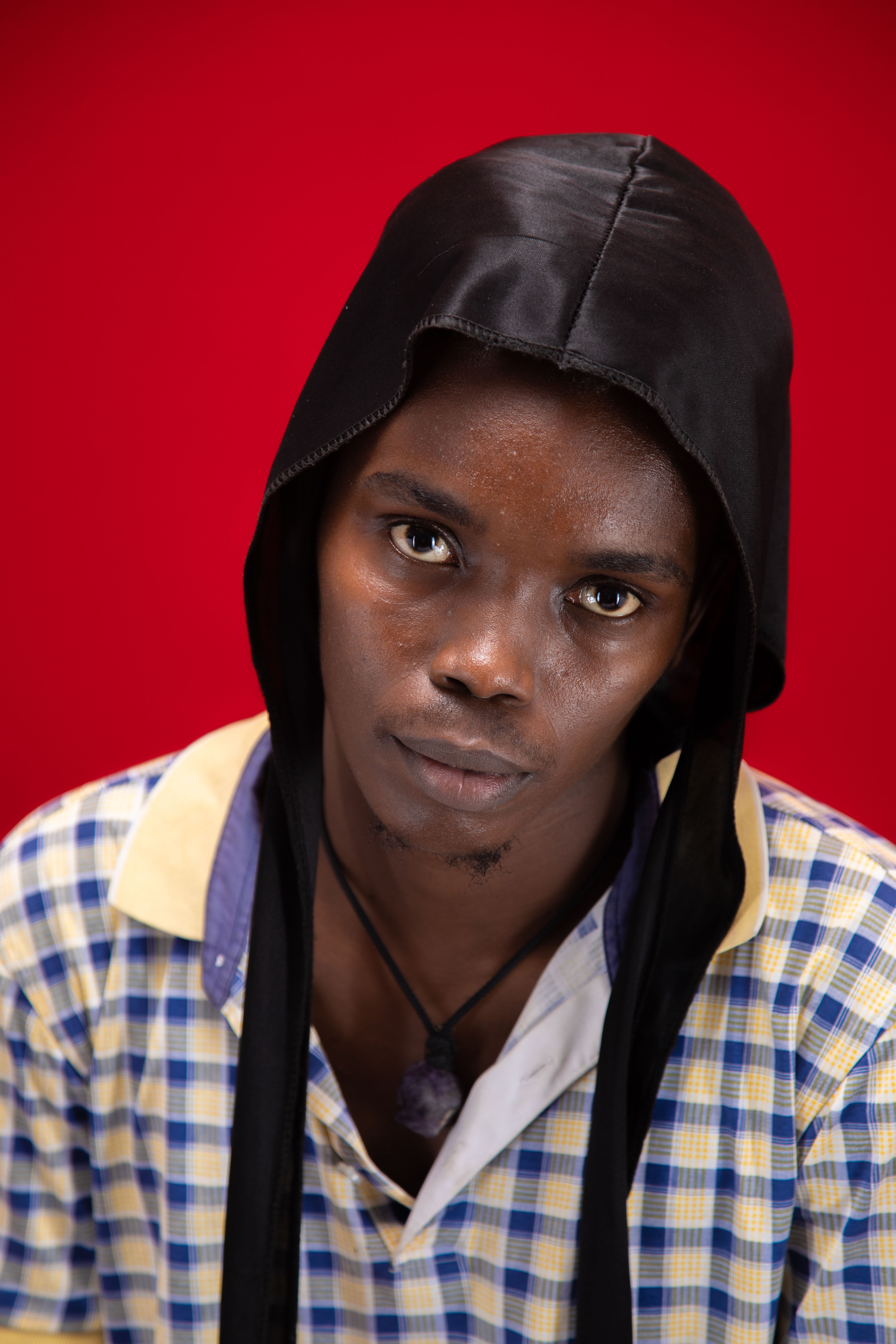 A striking portrait of a young man wearing a black durag against a red background.