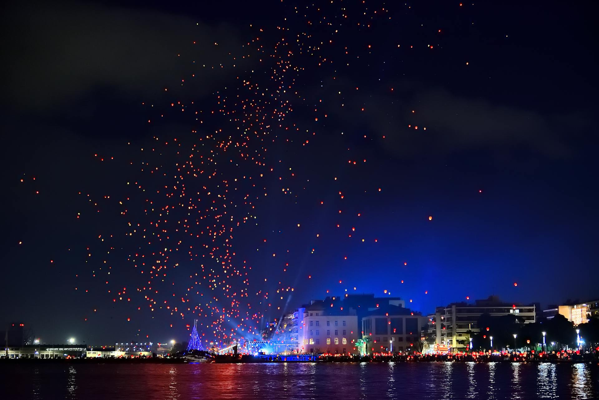 Colorful balloons rising over Volos waterfront at night, creating a vibrant and festive atmosphere near the sea.