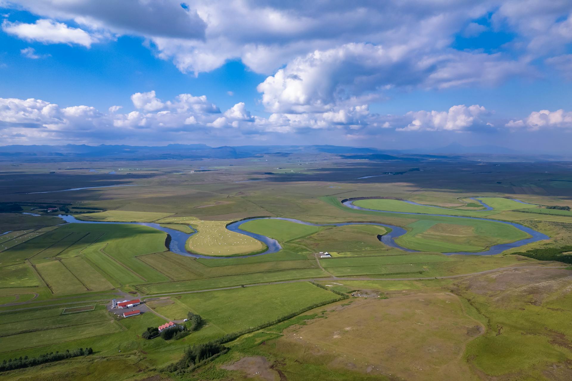 Stunning aerial view of Icelandic countryside with winding river and farmhouses in summer.