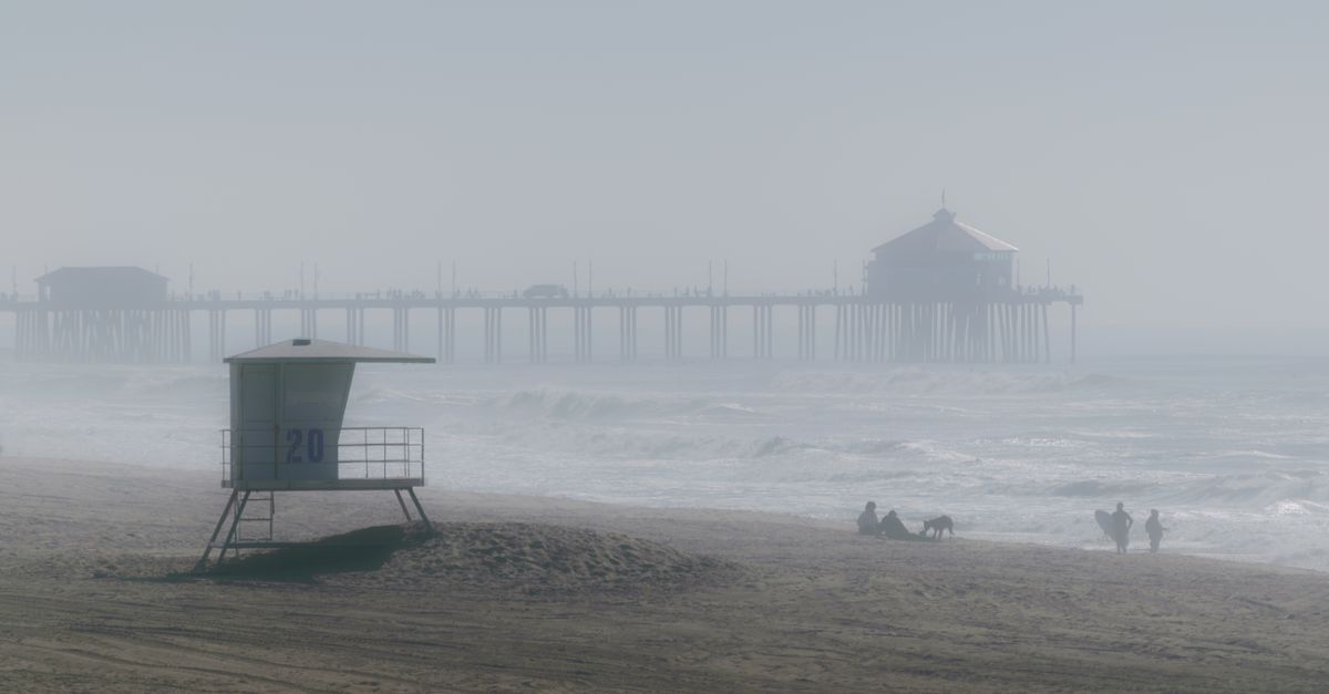 Misty morning view of a beach with a lifeguard tower and pier in the background.