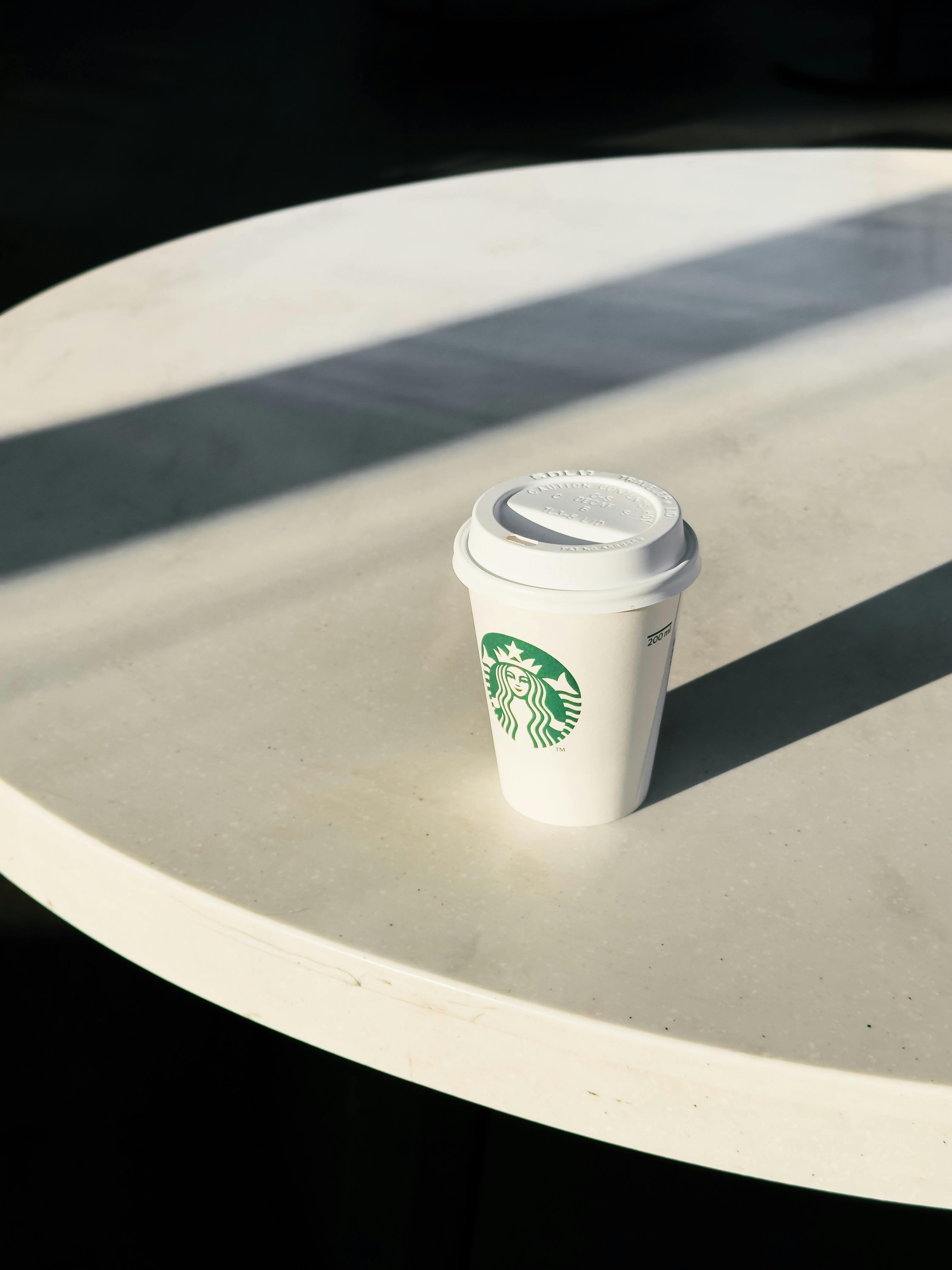 bezplatná Minimalistická fotografie značkového šálku kávy na kulatém stole s dramatickými stíny. Základová fotografie