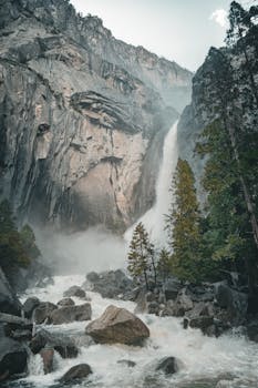 A stunning view of a waterfall cascading down cliffs in Yosemite National Park, surrounded by lush forest.