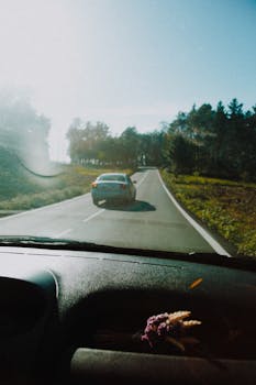 View from inside a car driving on a scenic rural road surrounded by trees, capturing a sense of travel and motion.