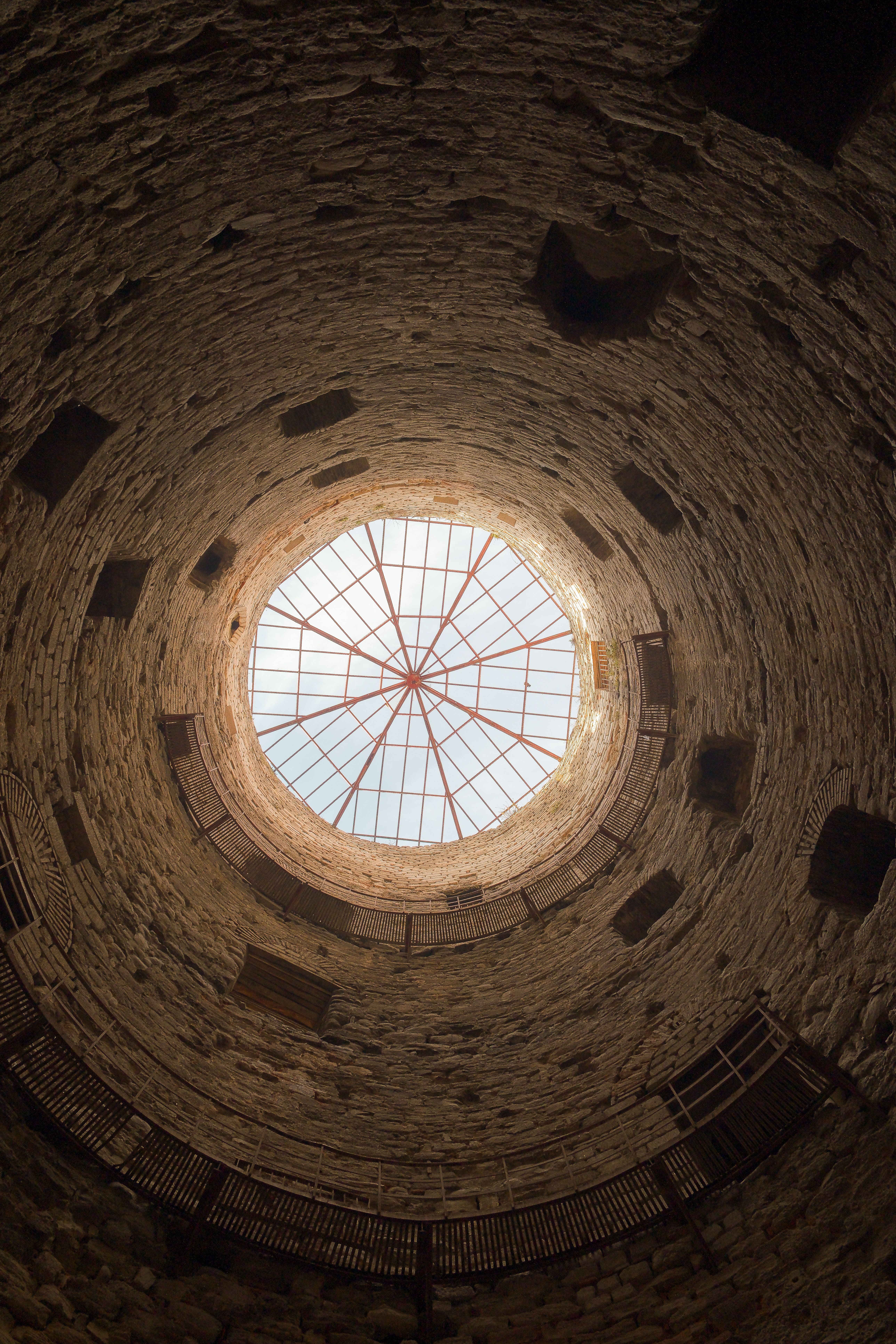 View from inside a stone tower looking up at circular skylight, architectural perspective.