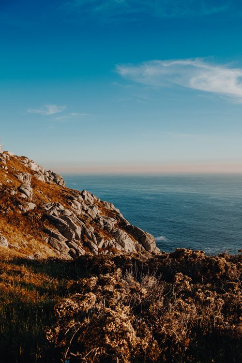 Free A breathtaking view of a rocky coastline under a vivid blue sky during sunset, showcasing the beauty of nature. Stock Photo