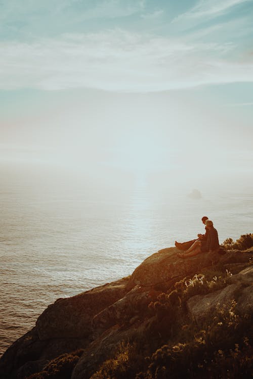 Two Persons Sitting on A  Cliff