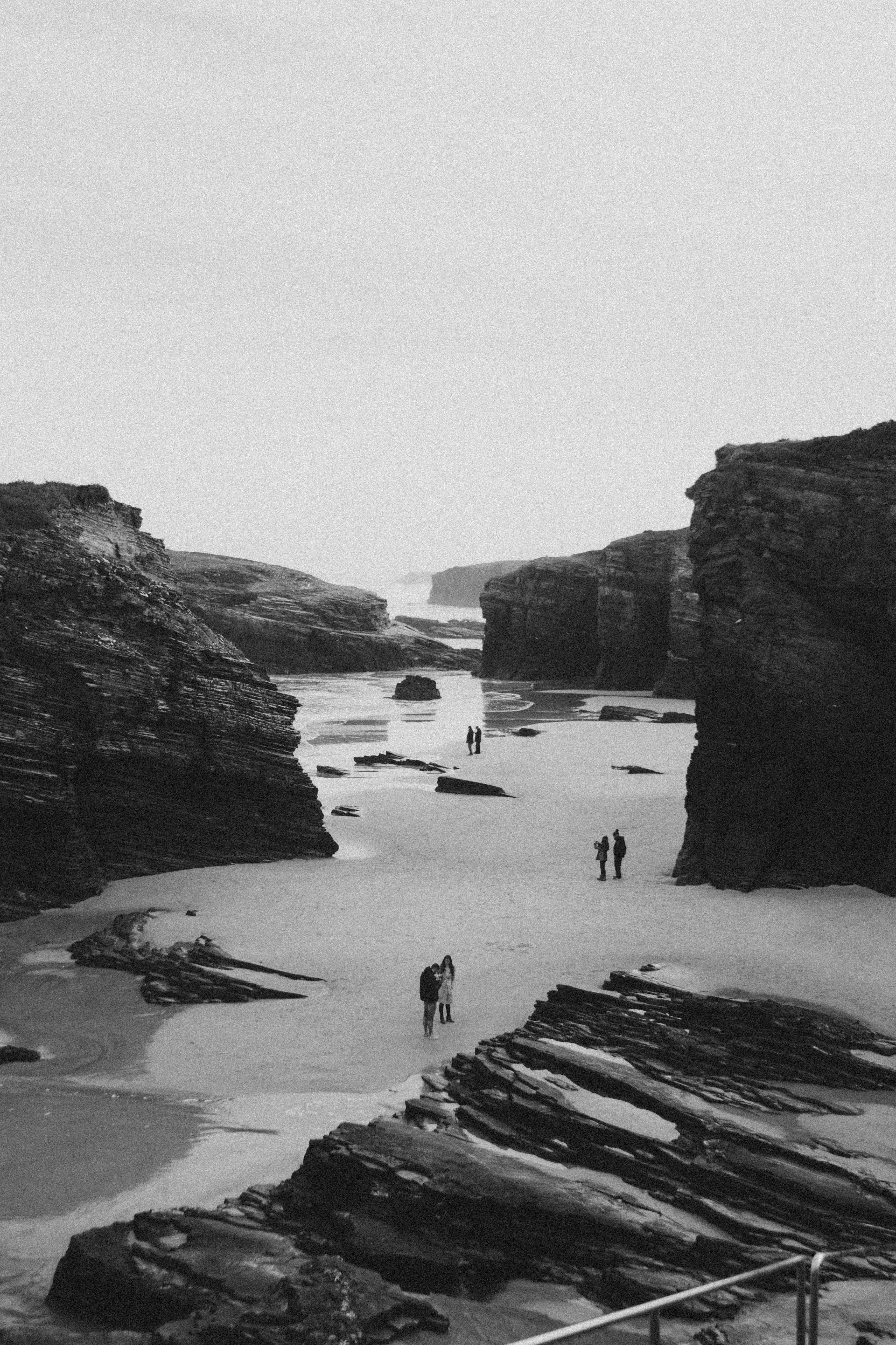 Black and white image of rocky coastal formations with people accentuating the vastness and tranquility.