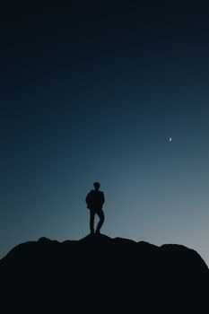 黄昏时分，山顶上一个人站在新月下的剪影