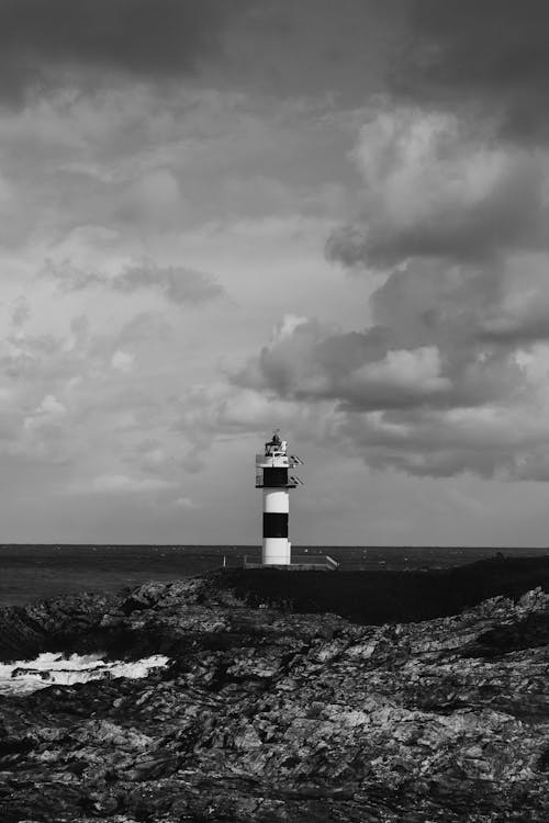 Grayscale Photo of Lighthouse Under Cloudy Sky