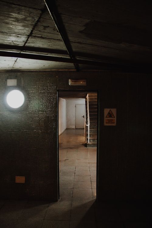 Free Explore the eerie and abandoned hallway through an open doorway with dim lighting and shadows. Stock Photo