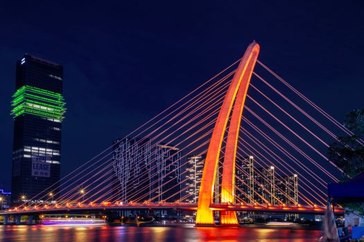 Stunning night view of a bridge illuminated in orange with modern city skyline and reflections.