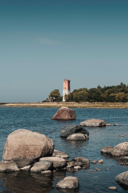 Tranquil landscape featuring a lighthouse behind coastal rocks and calm water.
