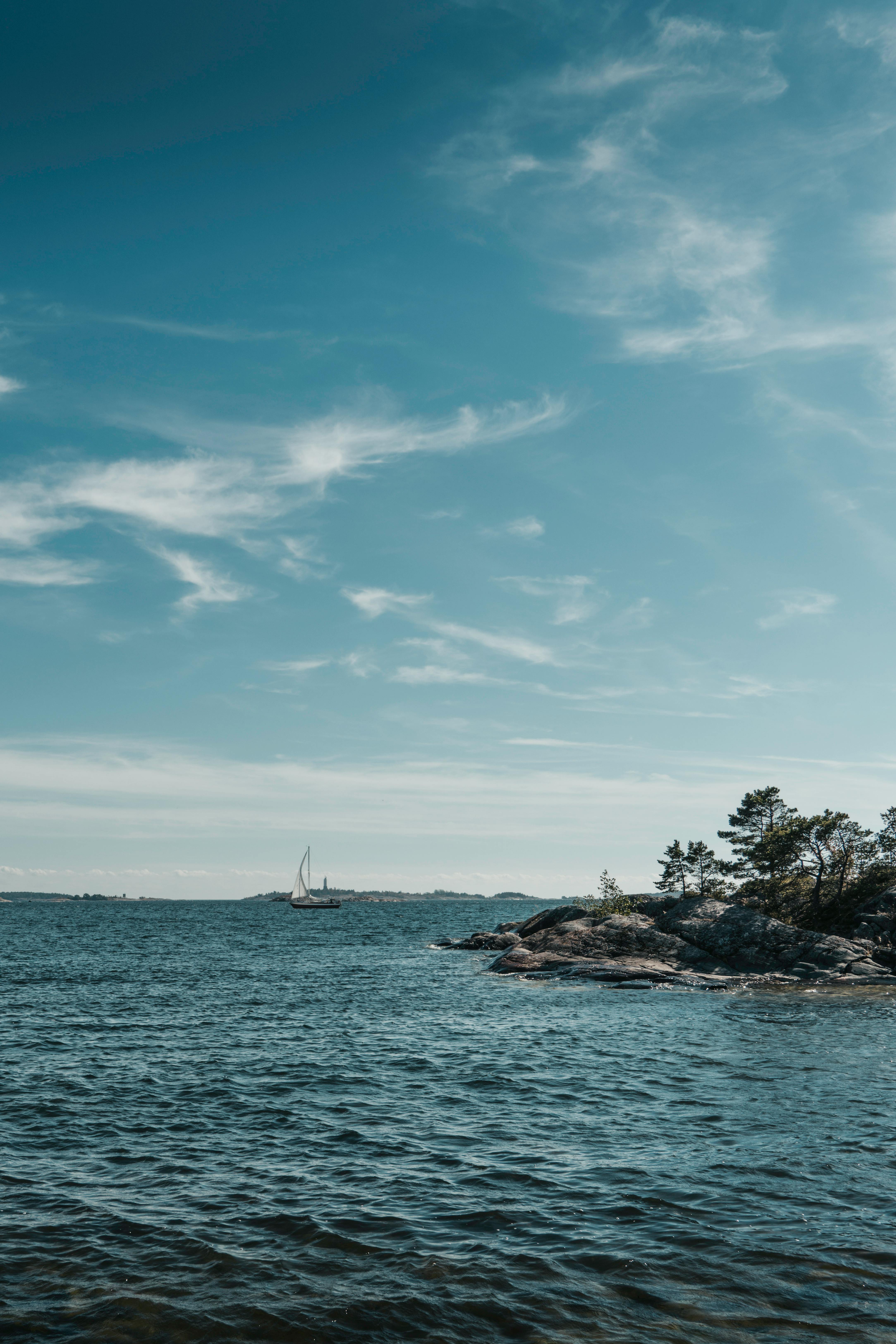 Tranquil view of a sailboat on the sea near a rocky shoreline under a clear blue sky.