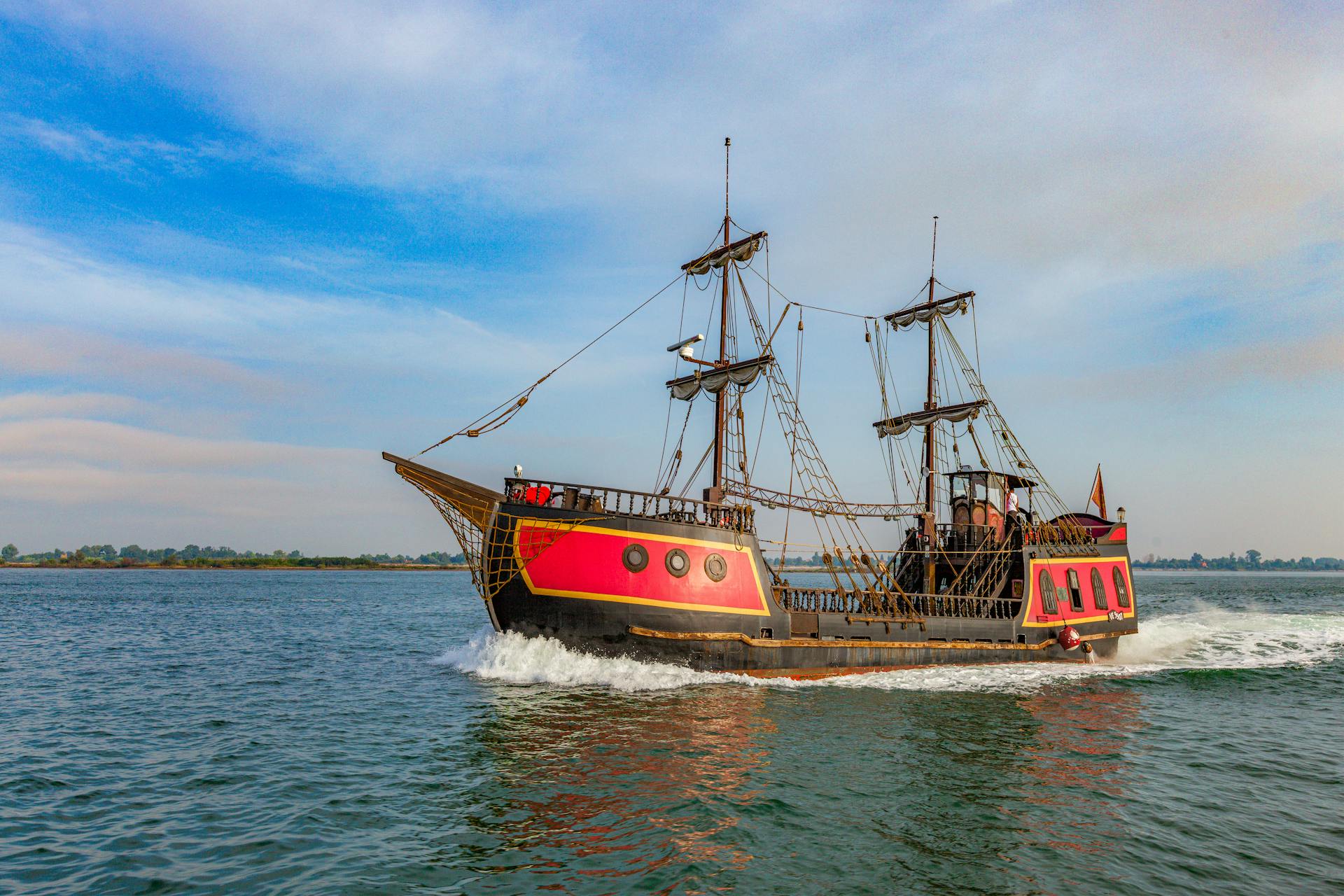 A vibrant pirate ship sails on a clear day, showcasing its vintage wooden structure and colorful design.