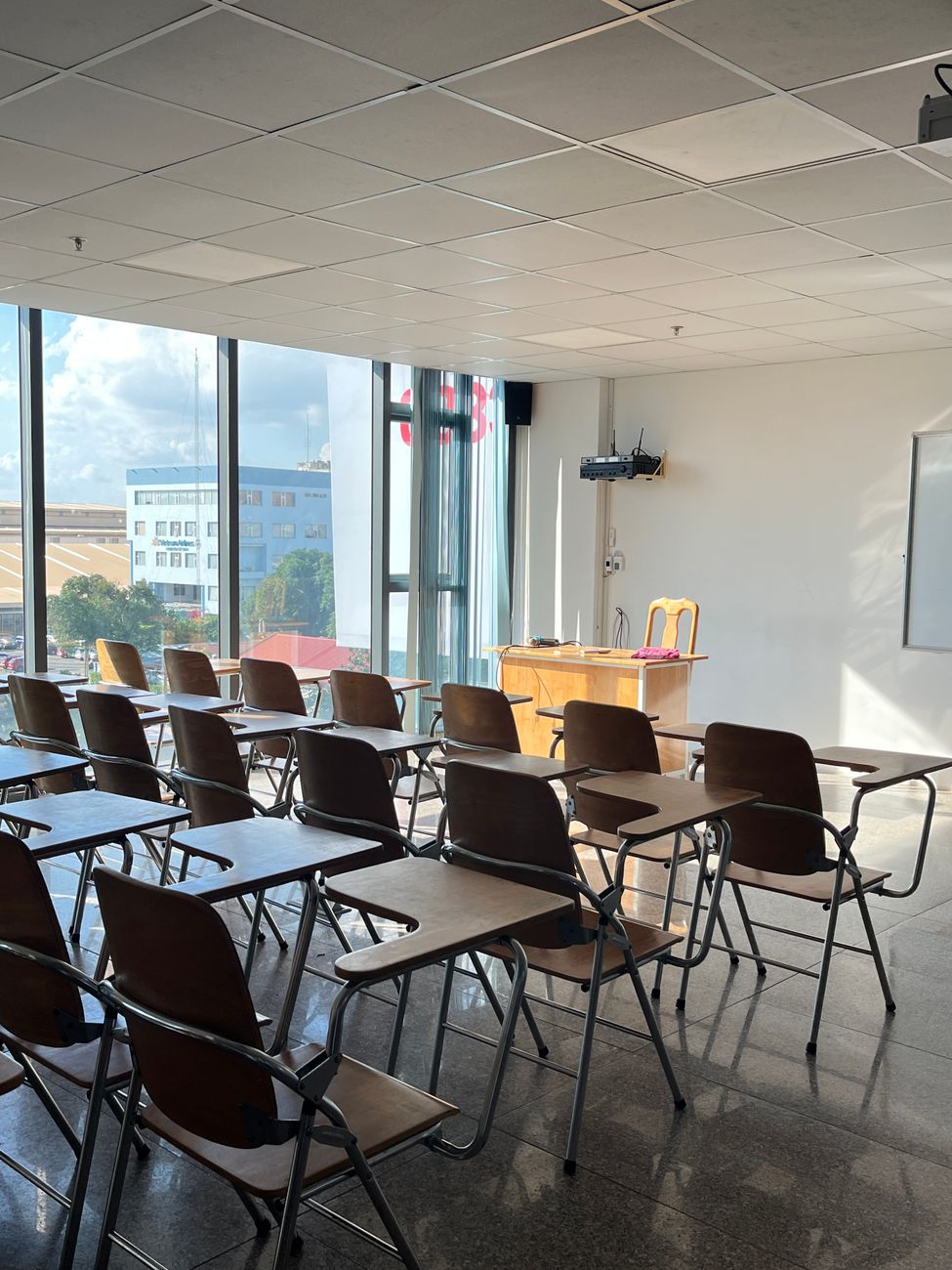 Heldere en lege klaslokaal met zonlicht dat door grote ramen stroomt, voorzien van houten bureaus en stoelen.