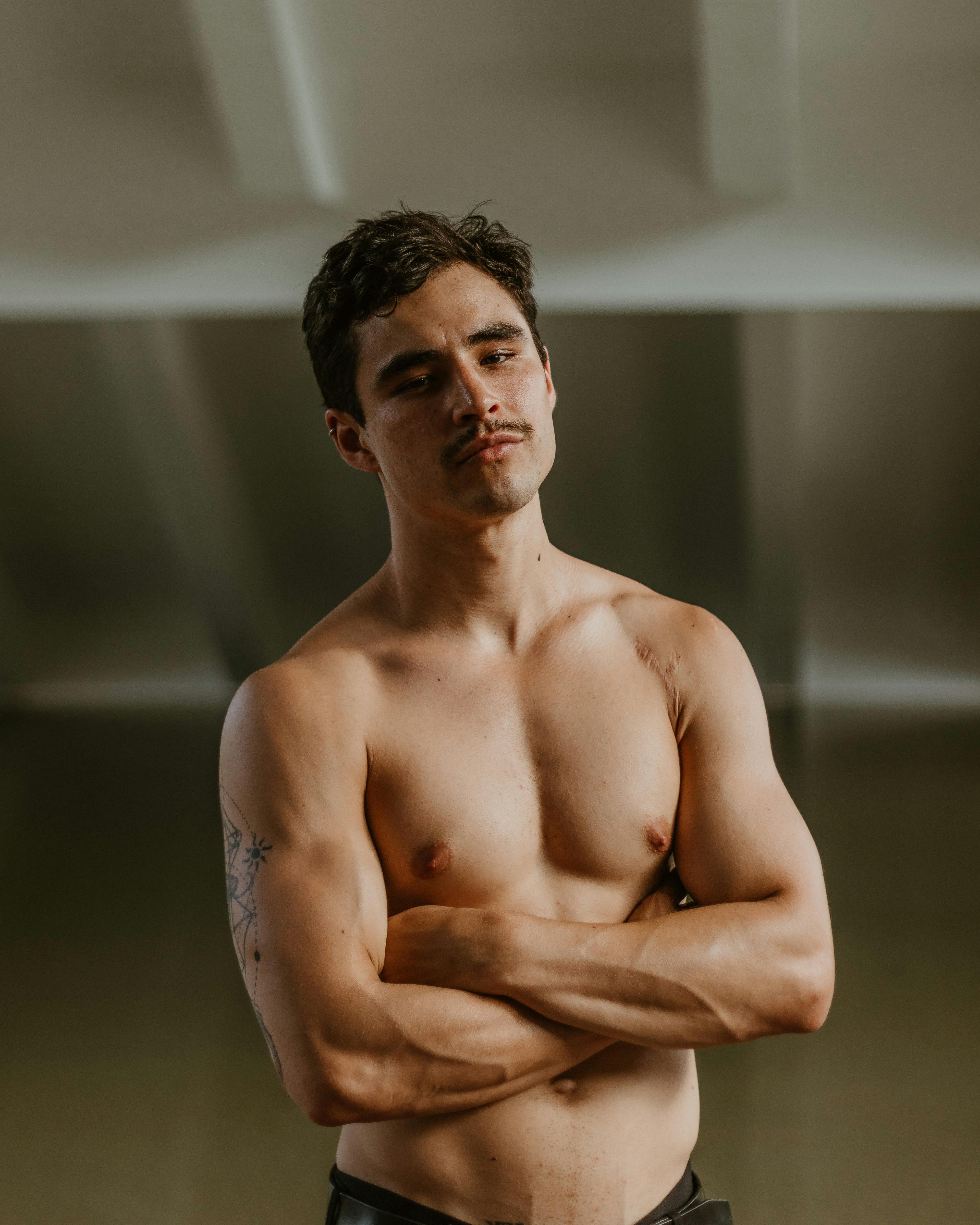 Gratis Potret model pria bertelanjang dada yang percaya diri berpose dengan tangan disilangkan di bawah cahaya alami. Foto Stok