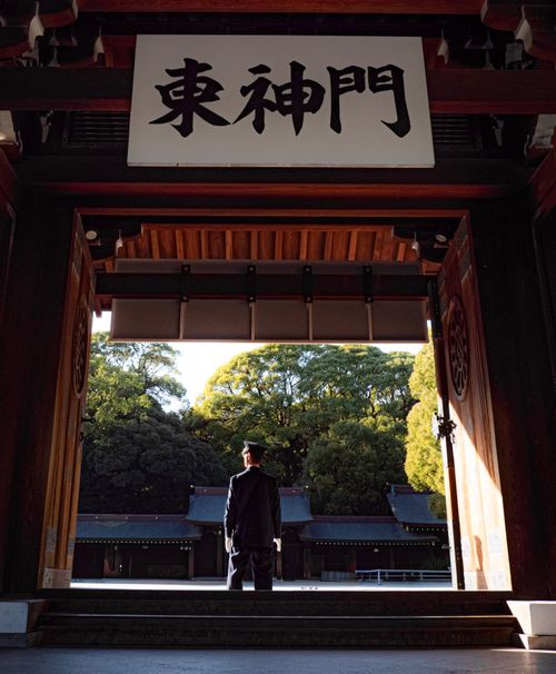 Free A lone guard stands at the entrance of a Japanese temple, surrounded by lush trees. Stock Photo