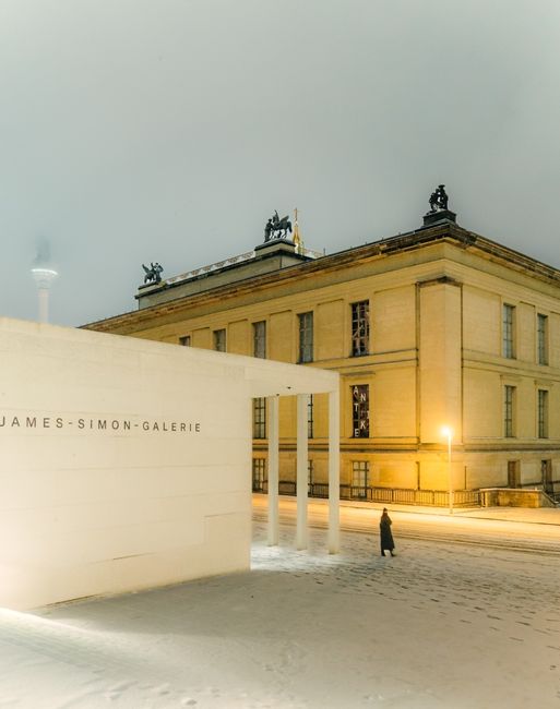 Snowy night scene of James-Simon-Galerie in Berlin with a lone pedestrian.