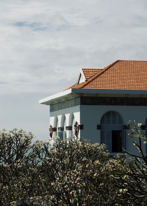 Free A vintage white building with an orange tiled roof and arched windows surrounded by flowering trees. Stock Photo