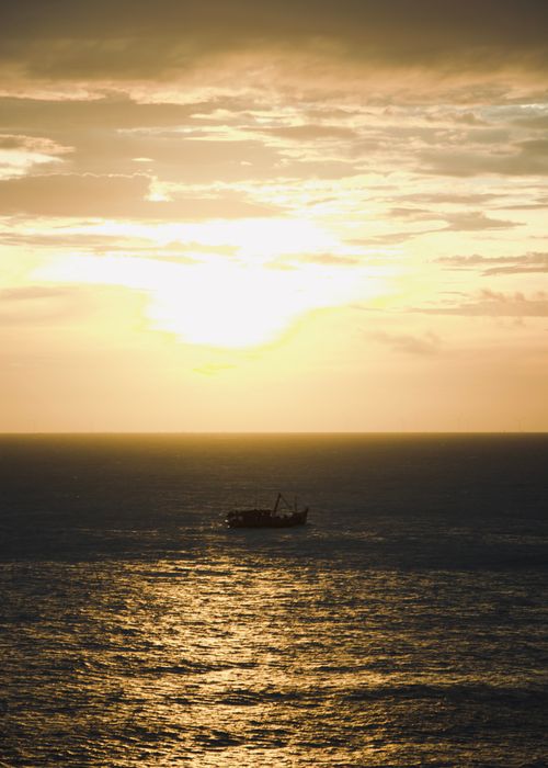 Free A breathtaking sunset over the ocean with a lone boat silhouetted on the horizon. Stock Photo