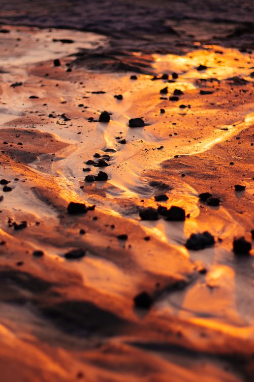 Free Beautiful sand and rock formations on the coastline during sunset, with rich orange and yellow hues reflecting on water. Stock Photo