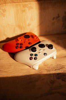 Red and white game controllers on wooden surface in warm light.