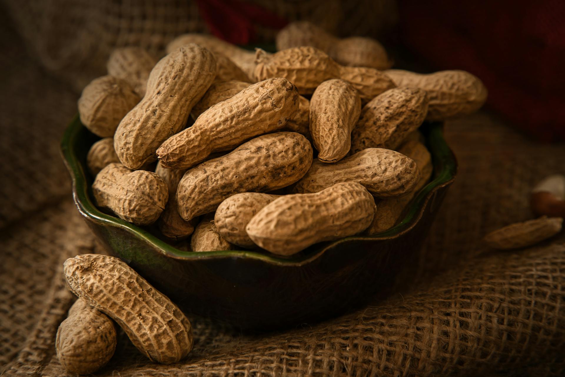 A rustic bowl filled with whole peanuts resting on a burlap cloth, evoking a natural and earthy feel.