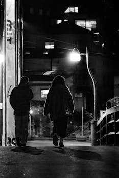 Monochrome night scene of two people walking in Sarajevo, highlighting urban life contrasts.