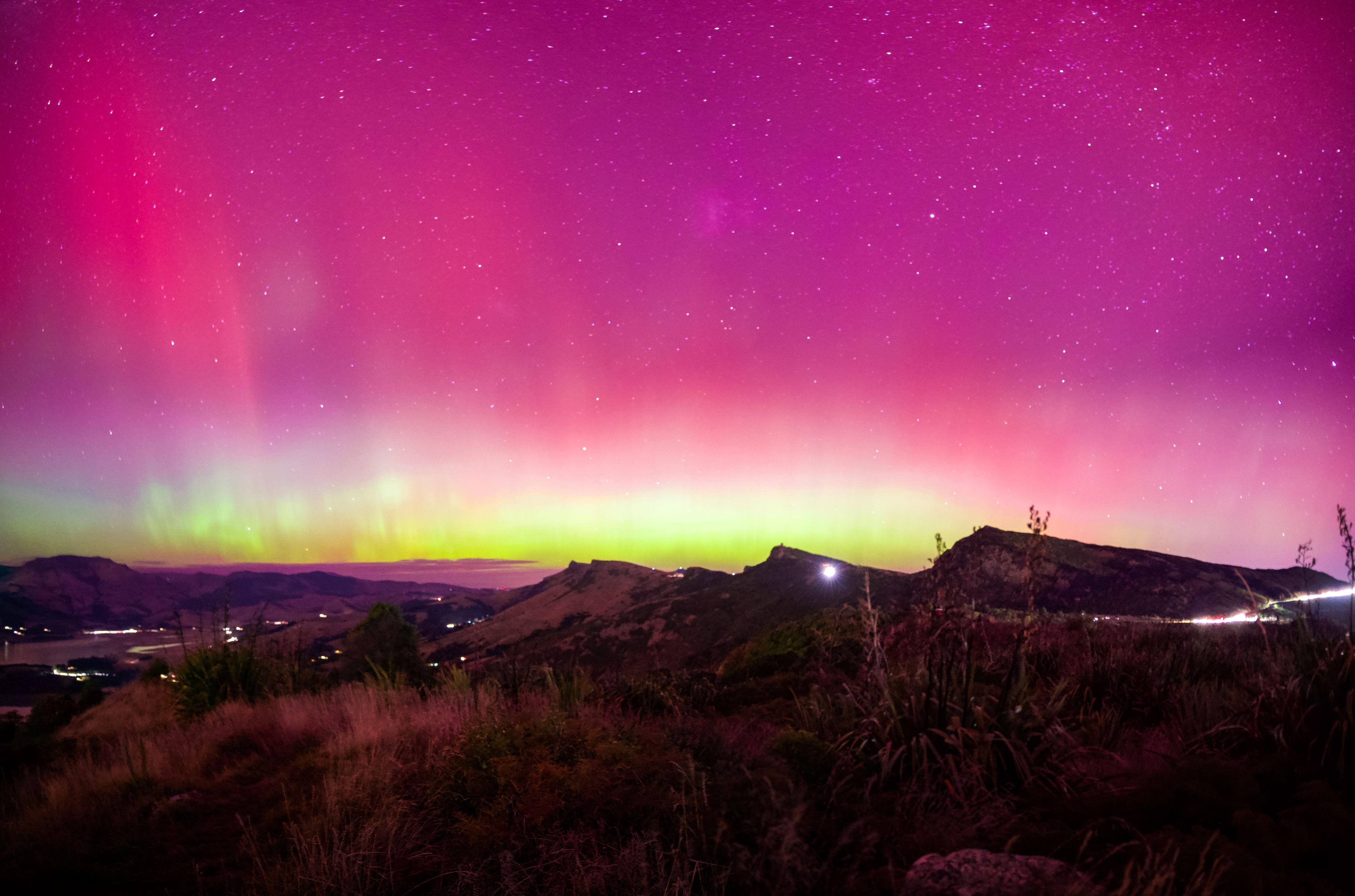 Aurora Australis berwarna merah muda dan hijau di langit malam di atas perbukitan Pulau Selatan, Selandia Baru