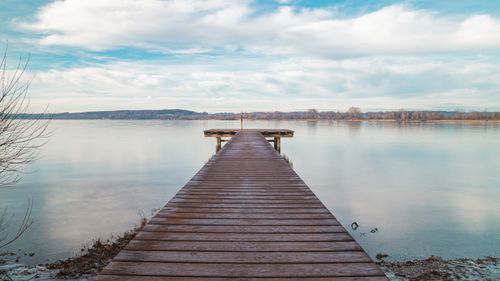 Free Peaceful wooden pier at Ammersee in Bavaria during winter, showcasing serene lake and sky reflections. Stock Photo