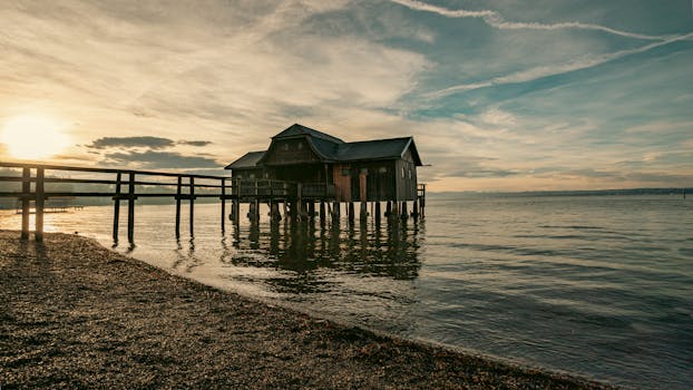 A peaceful boathouse with a walkway over Ammersee in Bavaria during sunset, creating a warm serene atmosphere.