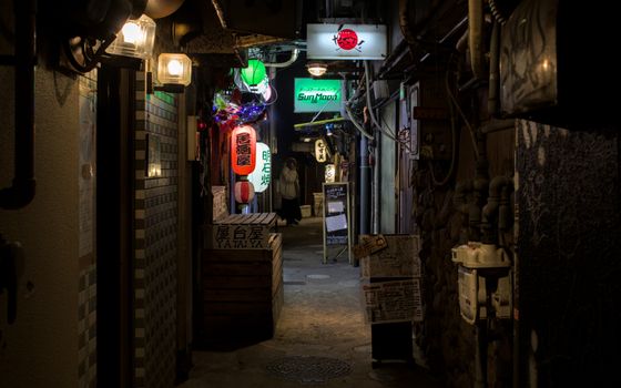 A dark alley in Osaka, Japan, featuring glowing lanterns and vibrant signs.