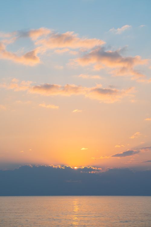 Free A tranquil sunrise over the ocean with soft clouds and pastel colors in the sky. Stock Photo